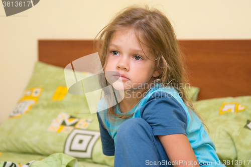 Image of Five-year sad sleepy girl waking up sitting on the bed