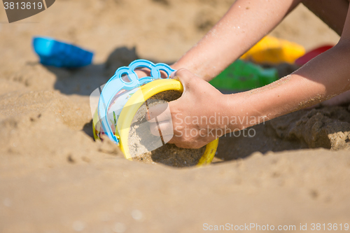 Image of The baby is gaining a bucket in the wet sand, close-up
