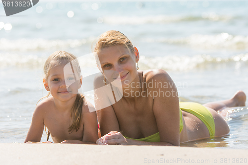 Image of Mom and daughter are in the four-year water on the sandy seafront and joyfully look to the Frame
