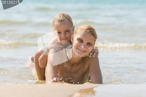 Image of Young woman with a daughter on his back lying on the beach and smiling