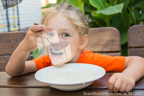 Image of Five-year girl with pleasure eats porridge for breakfast