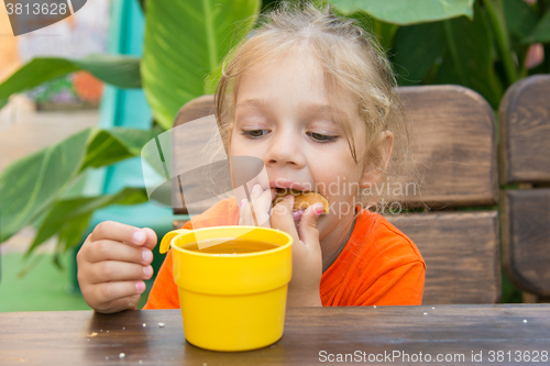 Image of Four-year girl funny stuffed bun in his mouth and looks at a glass of tea