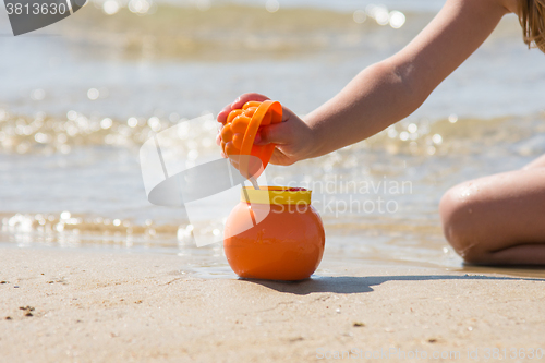 Image of Child sprinkles wet sand from the molds in a pot on the sandy beach seashore