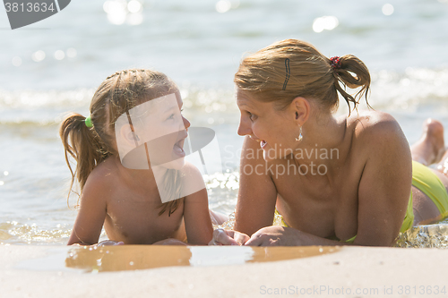 Image of Mom and daughter are in the four-year water on the sandy shore of the sea and happily looking at each other