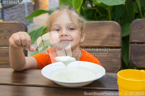 Image of Cheerful little girl eats porridge for breakfast