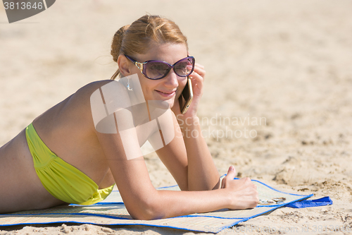 Image of Young girl lying on the sandy beach and happily talking on the phone