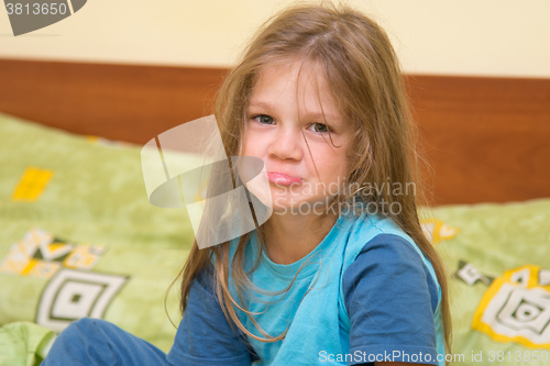 Image of Five-year girl waking up sitting on the bed and looks ridiculous in the frame