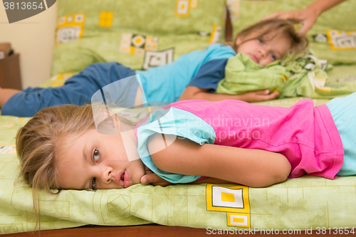 Image of Two girls lie on a bed on the opposite sides