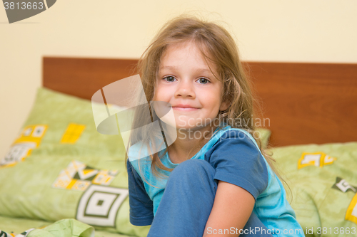 Image of Funny five-year girl sitting on a bed waking up