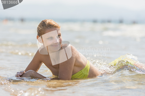 Image of Young beautiful girl lying in shallow water at the seaside, and looks into the distance