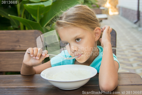 Image of Upset six year old girl slowly eating porridge for breakfast