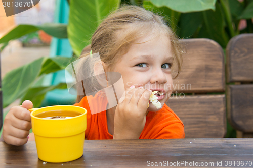 Image of Hungry funny girl biting bun and drinking tea