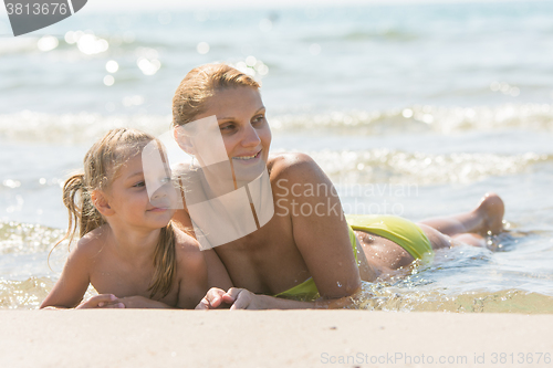 Image of Mom and daughter are in the four-year water on the sandy shore of the sea and looking happily along the coast of the sea