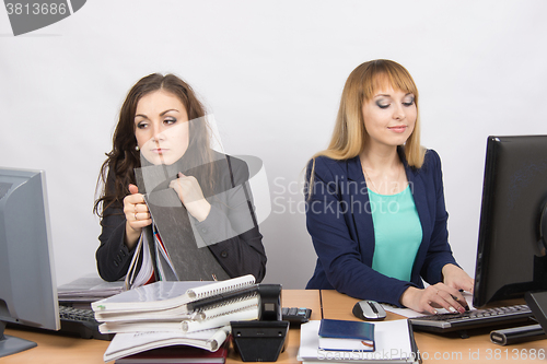 Image of Female colleagues in the office, a tired looking in the monitor, the other happy working on a computer