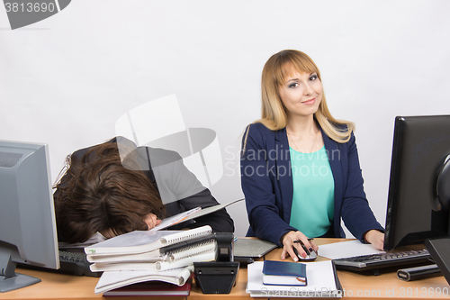 Image of Female colleagues in the office, one had fallen asleep on a pile of folders, the other works in the computer and looked in the frame