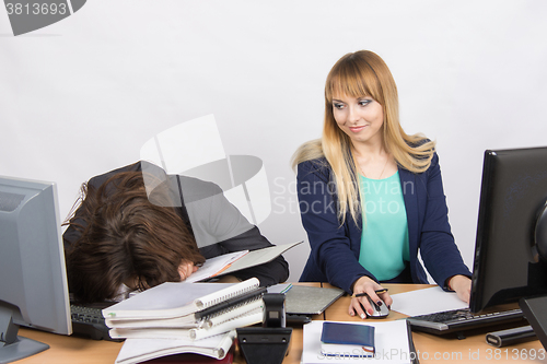 Image of Female colleagues in the office, one had fallen asleep on a pile of folders, and the second looked at her