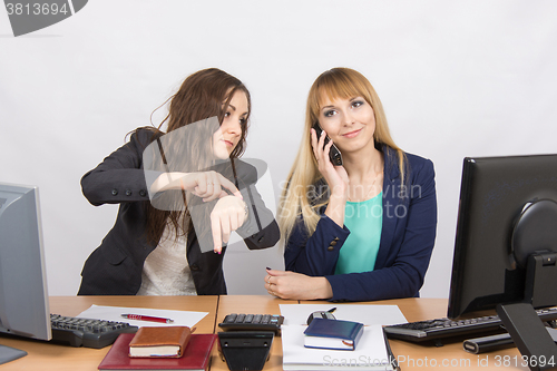 Image of The situation in the office - the employee shows to watch that for a long time colleague talking on the phone