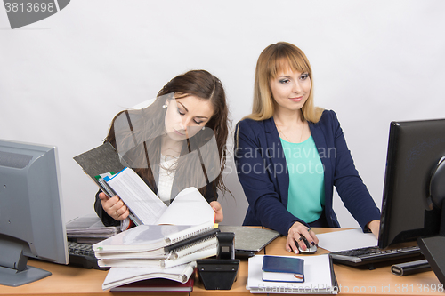Image of Female colleagues in the office, one works with paper documents, the second computer with electronic
