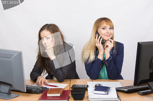 Image of The situation in the office - happy employee talking on phone, colleague looking wearily at the computer screen