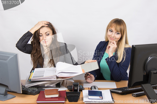 Image of The situation in the office - one employee watching folders with documents and clutched her head, and the second looks at laptop