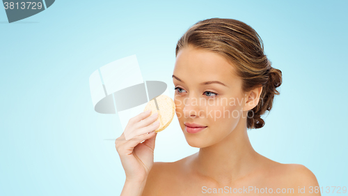 Image of young woman cleaning face with exfoliating sponge