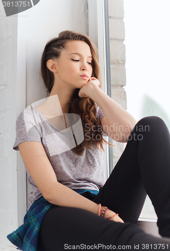 Image of sad pretty teenage girl sitting on windowsill