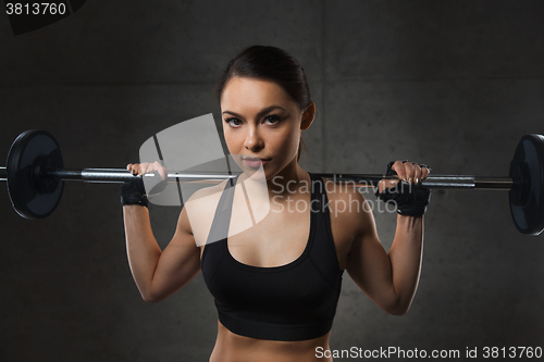 Image of young woman flexing muscles with barbell in gym