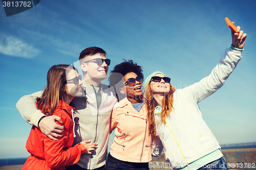 Image of smiling friends taking selfie with smartphone