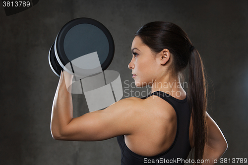 Image of young woman flexing muscles with dumbbells in gym