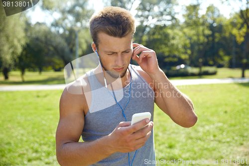Image of young man with earphones and smartphone at park