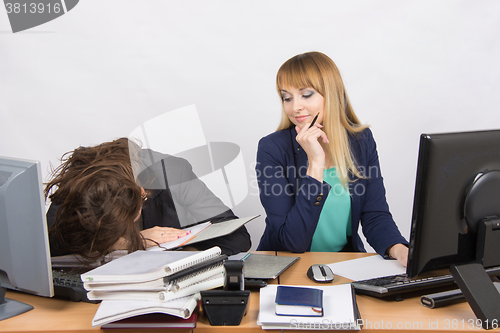 Image of Female colleagues in the office, one had fallen asleep on a pile of folders, the second with a sneer looks at her