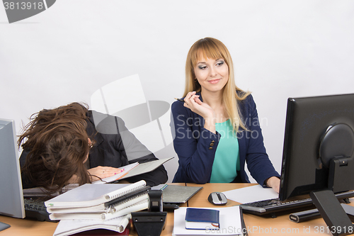 Image of Female colleagues in the office, one had fallen asleep on a pile of folders, the other happily looking at the monitor screen