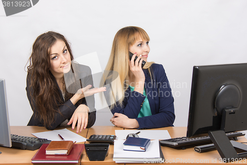 Image of The situation in the office - one employee on the phone, the other asks for her phone