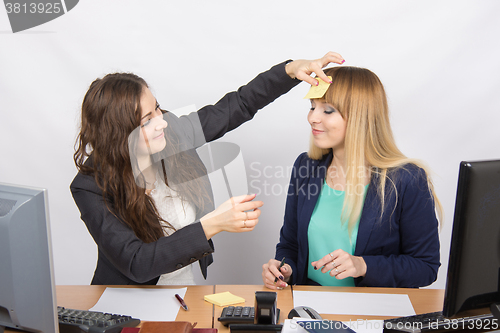 Image of An employee of the office glues note with the drawn sun on the forehead of his colleague