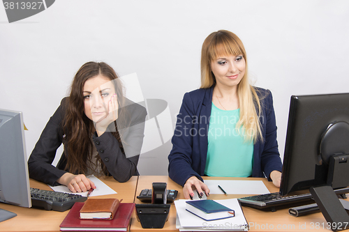 Image of The situation in the office - a woman sitting at a table in frustration, the other happily looking at a computer screen