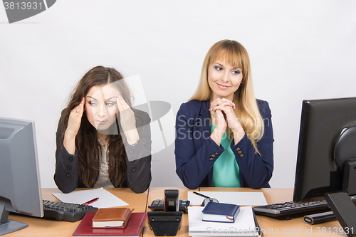 Image of The situation in the office - girl happily looking at a computer screen, the other a girl with a headache looking at the screen