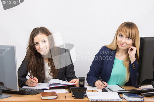 Image of Two business women writing in paper documents sitting at a desk and looked in the frame