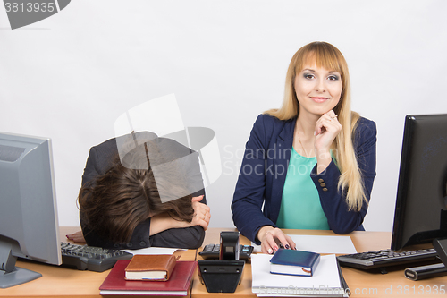 Image of  The situation in office - frustrated woman lay on the table, her colleague happily looks into the frame