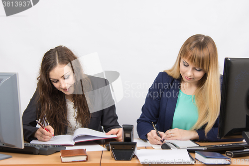 Image of Two business women writing in paper documents sitting at a desk
