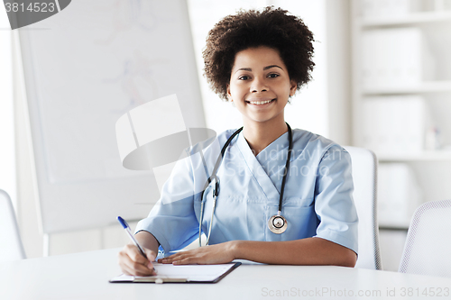 Image of happy female doctor or nurse writing to clipboard