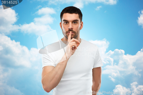 Image of young man making hush sign over blue sky