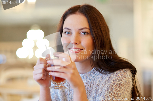 Image of smiling young woman drinking tea at cafe