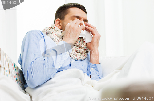Image of ill man blowing nose with paper napkin at home