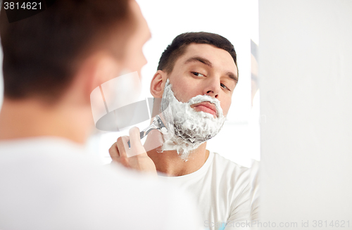 Image of man shaving beard with razor blade at bathroom