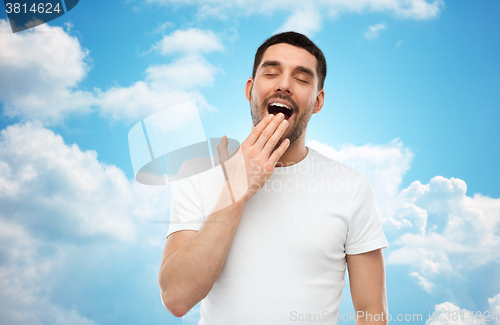 Image of yawning man over blue sky background