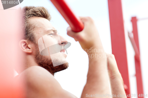 Image of young man exercising on horizontal bar outdoors