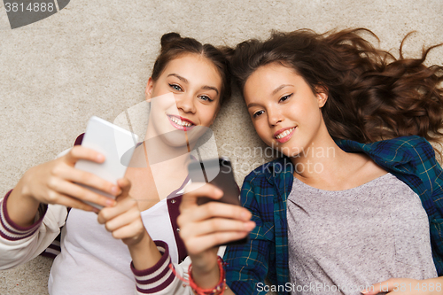 Image of happy teenage girls lying on floor with smartphone
