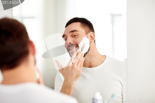 Image of happy man applying shaving foam at bathroom mirror