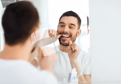 Image of man with dental floss cleaning teeth at bathroom