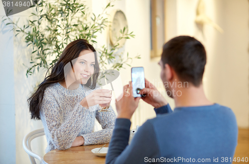 Image of man taking picture of woman by smartphone at cafe